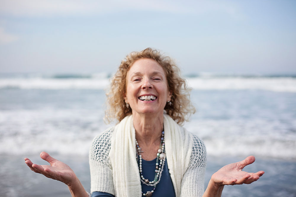 Amy Weintraub with arms open in front of the ocean